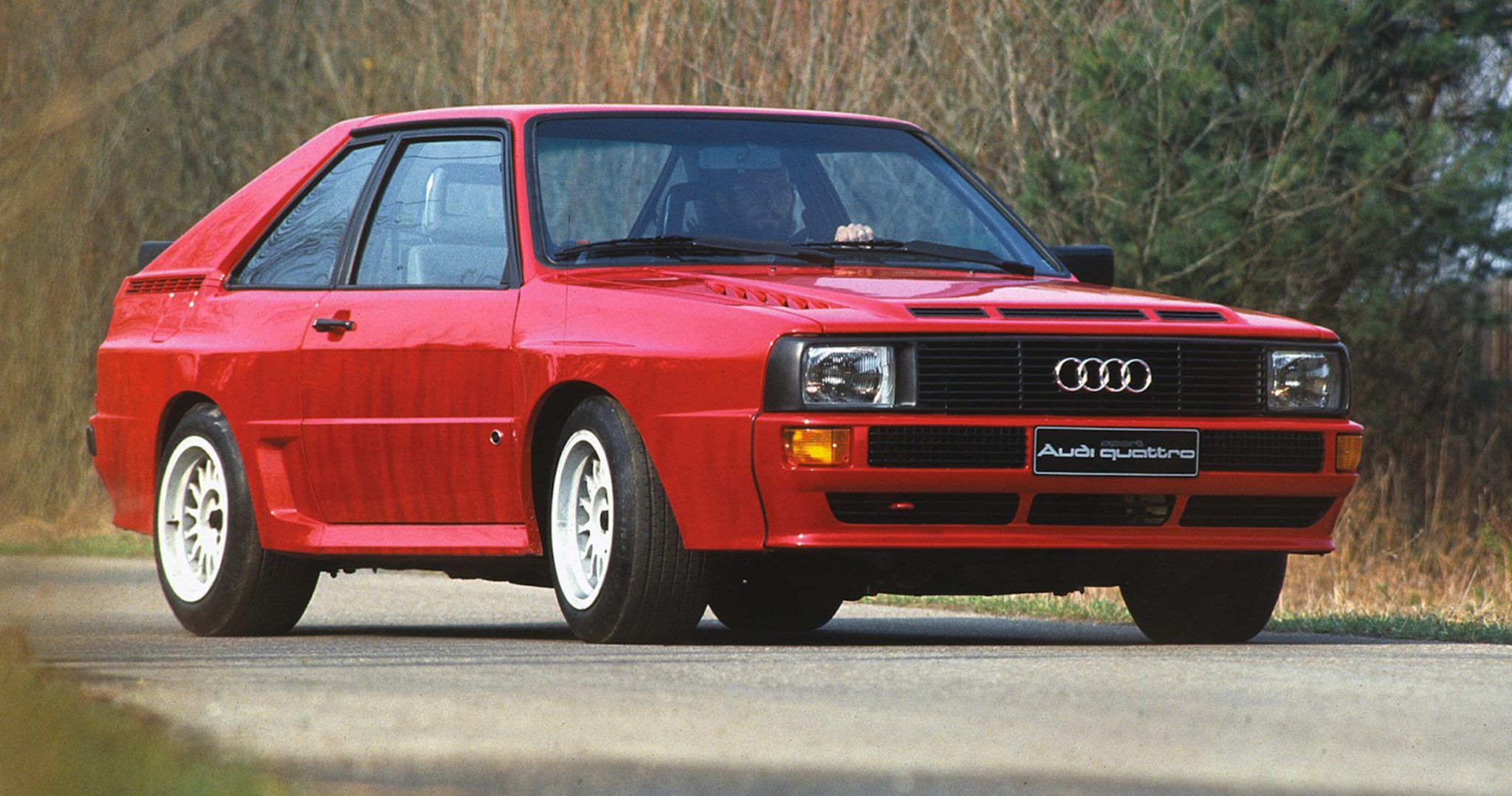 A side view of a red 1980 Audi Quattro Coupe on a road.