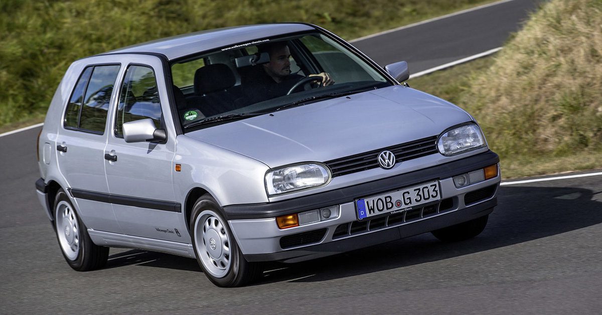 A side view of a rider enjoying a drive on a twisty road with his Silver four-door MK3 VW Golf