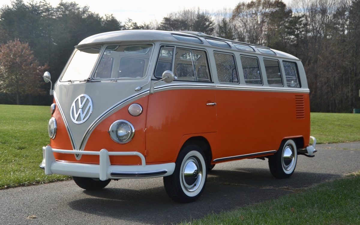 A side view of a first-gen orange VW Bus on an old asphalt road