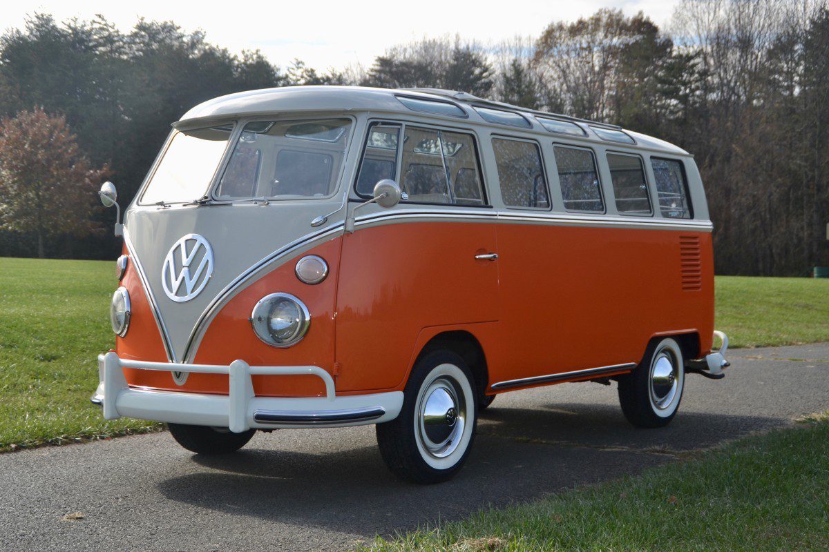 A side view of a first-gen orange VW Bus on an old asphalt road