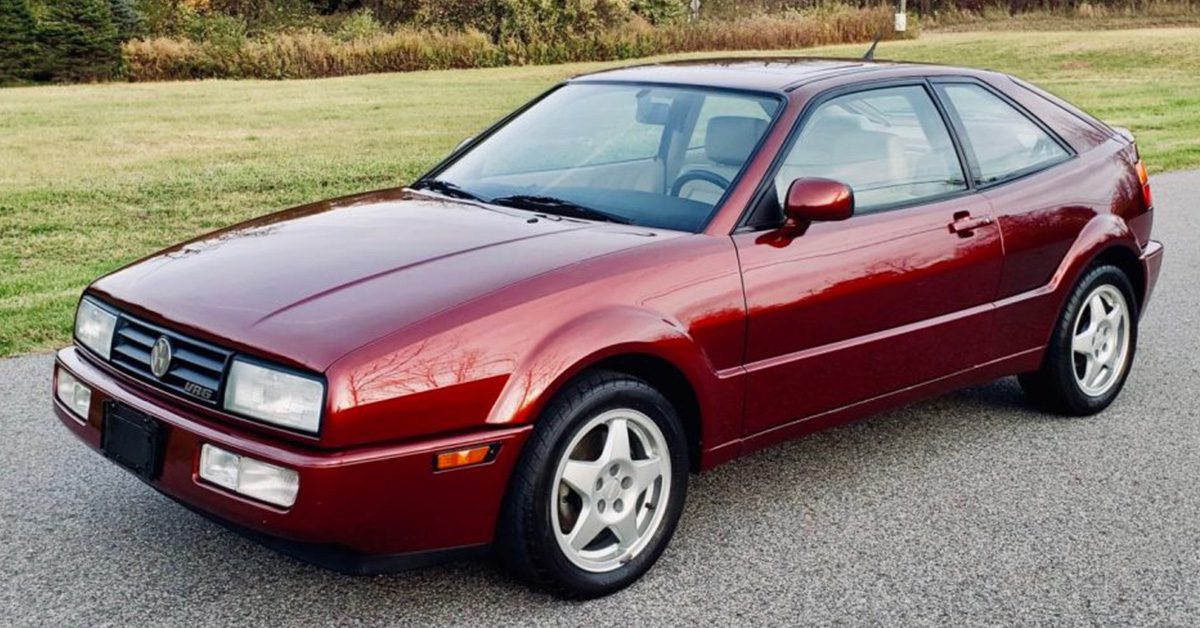 A side view of a 1994 burgundy VW Corrado SLC VR6 on a stretch of road next to a garden