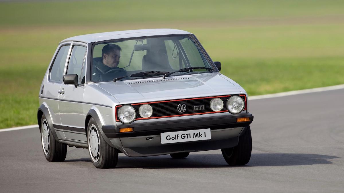 A side view fo a Silver MK1 VW Golf GTi on a stretch of road next to a field