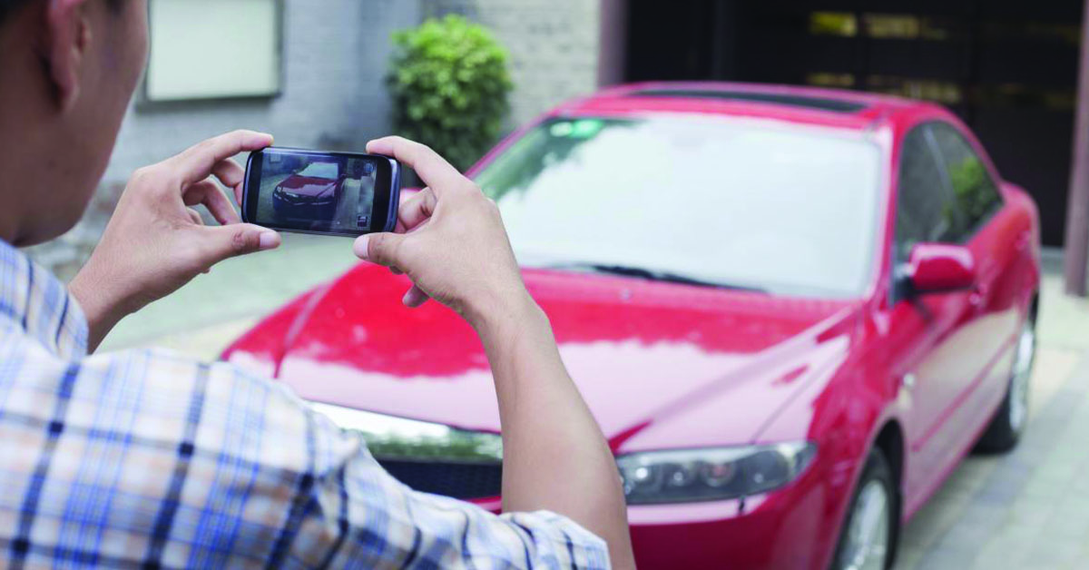 A guy taking photos of a car with a cell phone