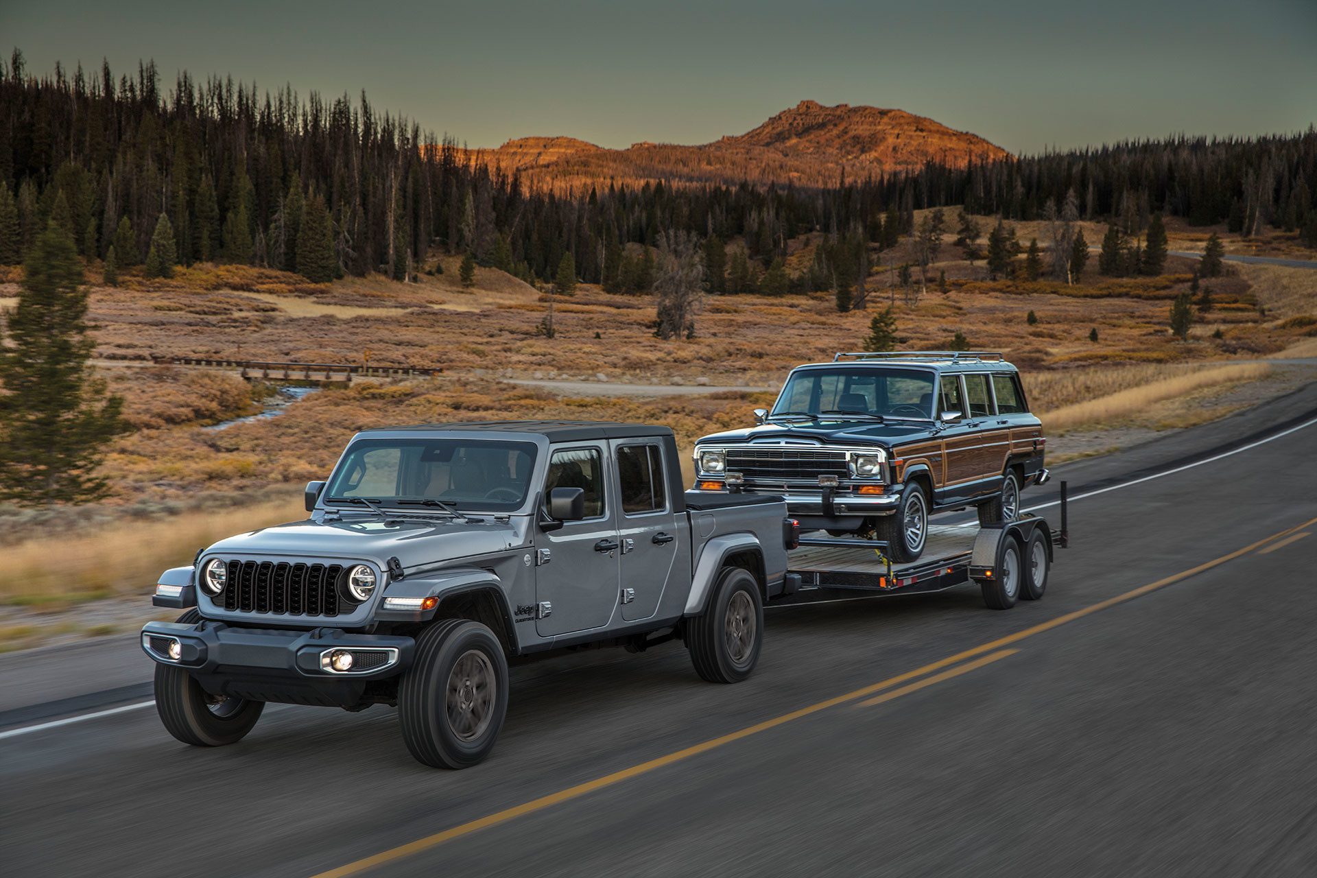 Three-quarter front view of a 2023 Jeep Gladiator pulling a Jeep Wagoneer on a trailer