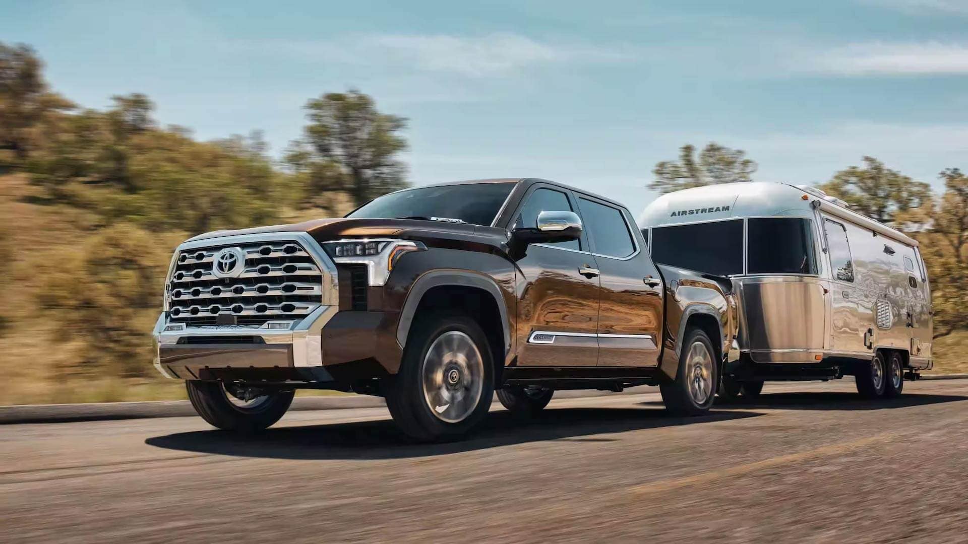 Three-quarter front view of a 2023 brown Toyota Tundra pulling a trailer