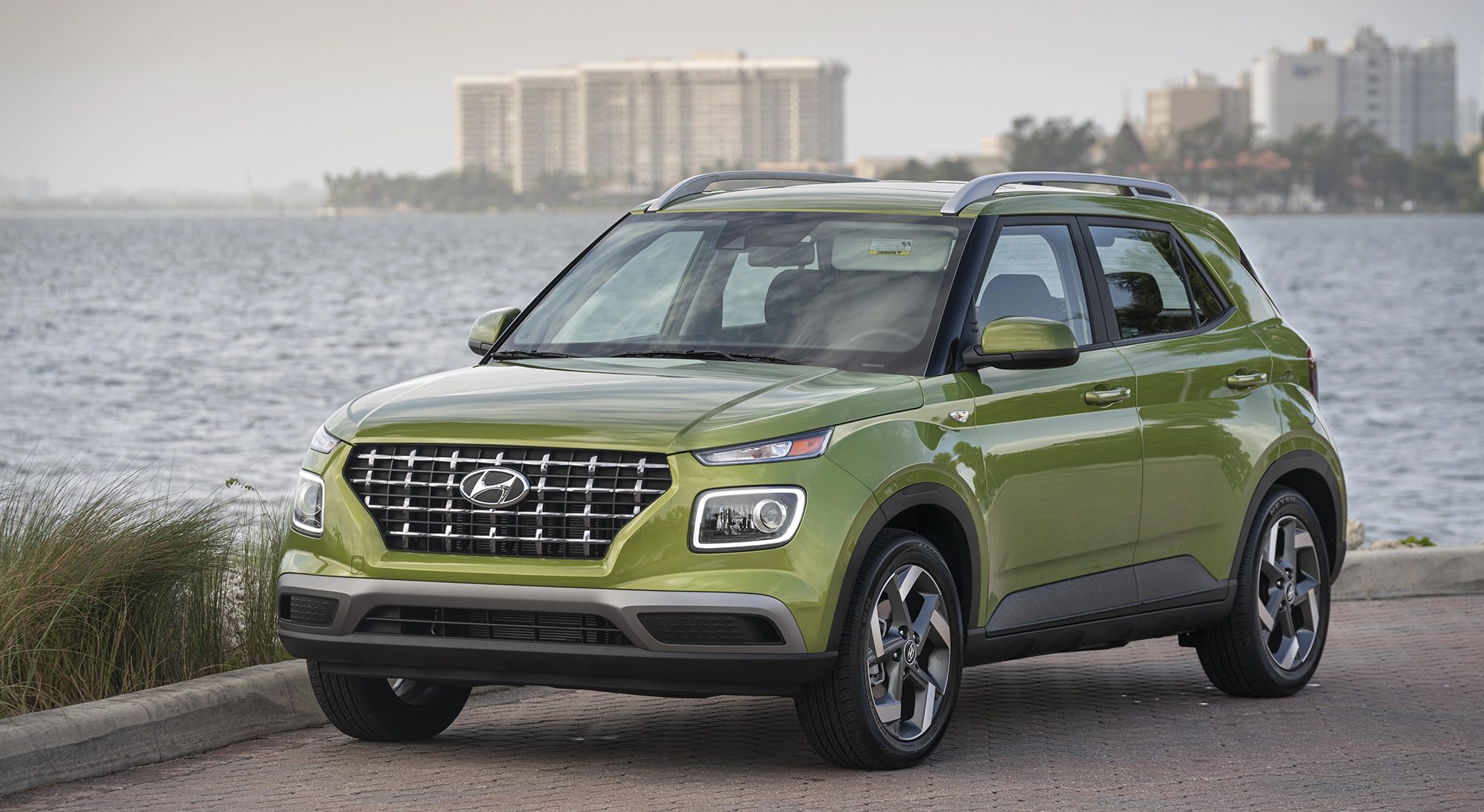 Three-quarter front view of a 2024 green Hyundai Venue with water background