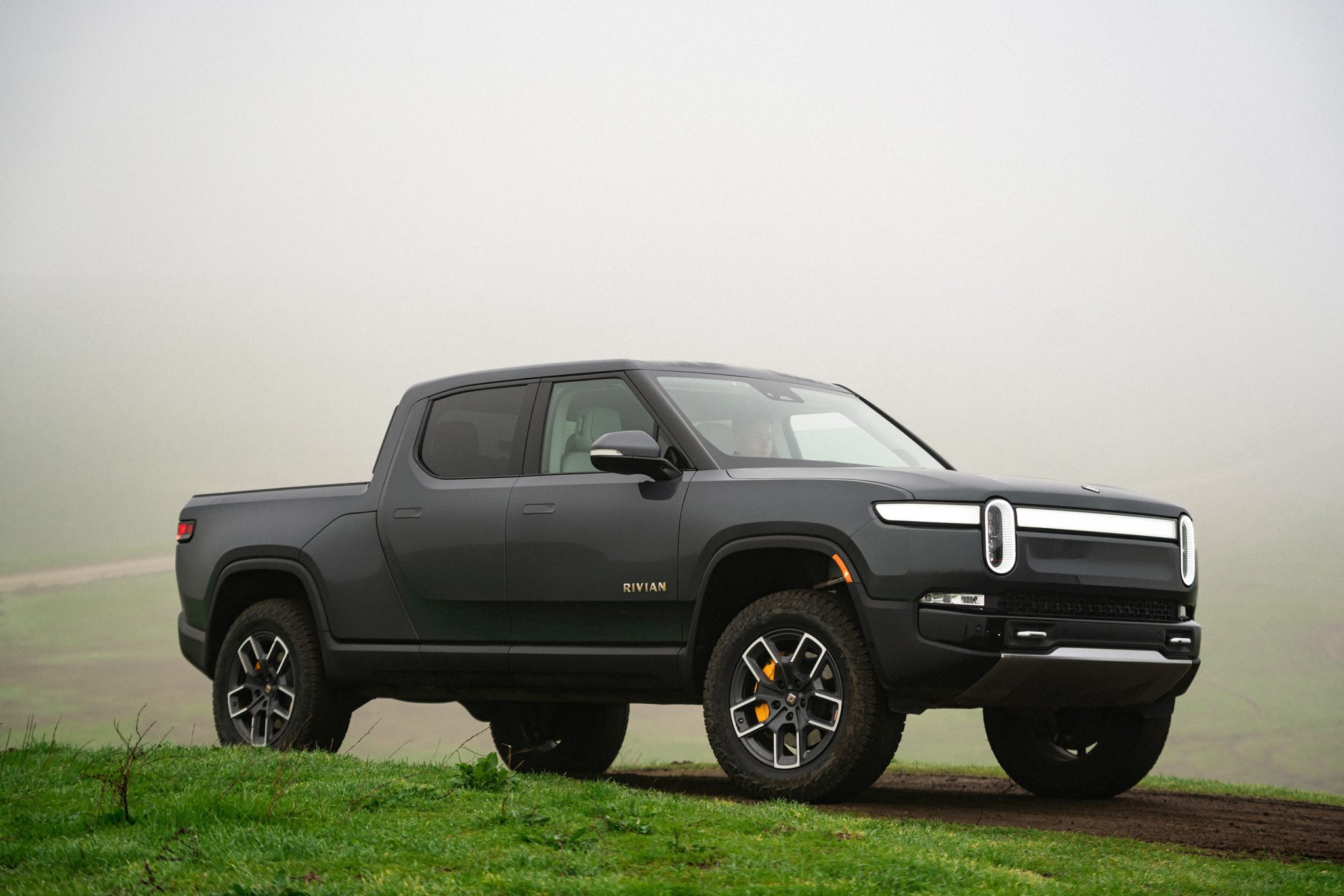 Side view of a 2024 black Rivian R1T on a hill